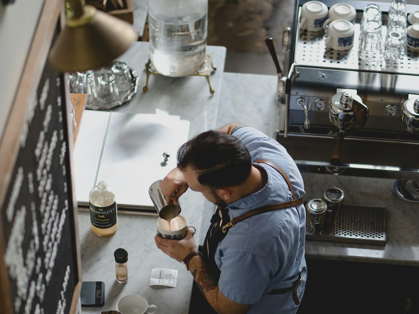 Barista at a coffee shop counter, hourly employees clock in on a Kloqk tablet kiosk in seconds
